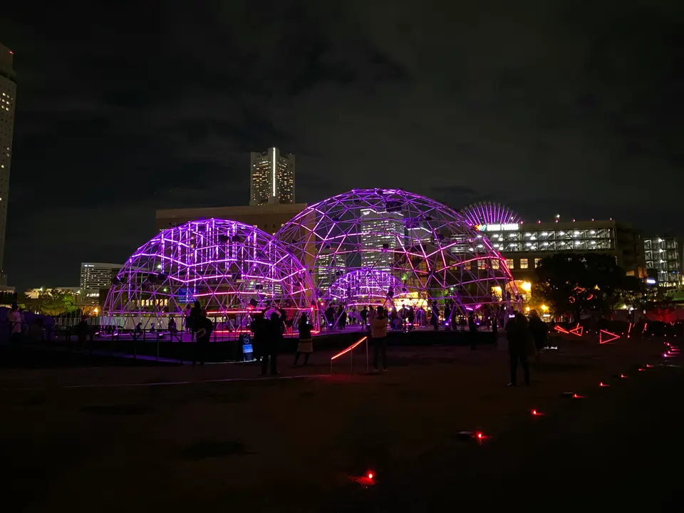 紫とピンクの光に包まれた「CROSS DOME」。横浜ランドマークタワーを背景に浮かぶ夜景