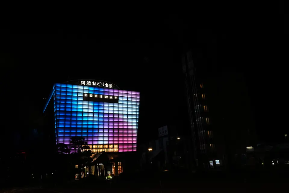 格子状のファサードが青からマゼンタへとグラデーションする、夜の阿波おどり会館のLED景観照明