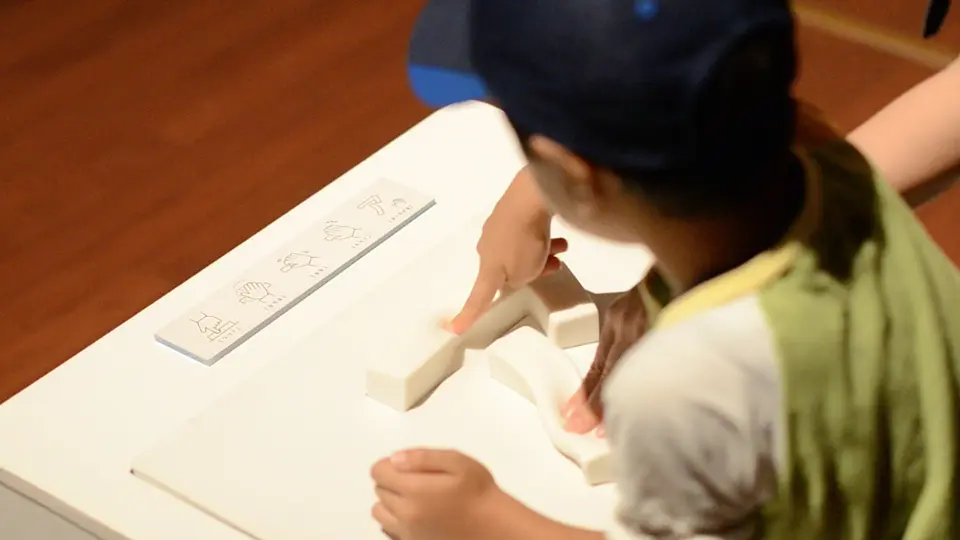操作方法を示すカードの横で「あ」の立体物に指で触れる子供