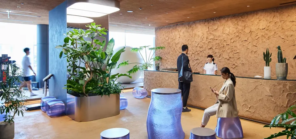 Personal Wellness Clinic MARUNOUCHIの受付ラウンジ。石調の壁と観葉植物、青みを帯びたスツールが並ぶ空間