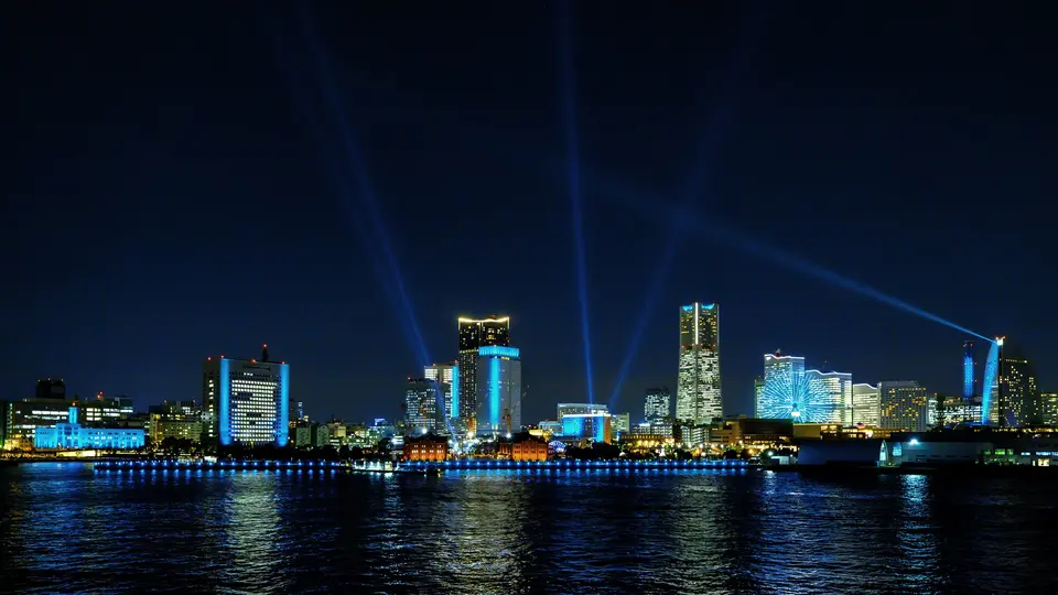 横浜の夜景に、複数のサーチライトが交差して伸びる「ヨルノヨ 2021 – FLOW –」の光の演出