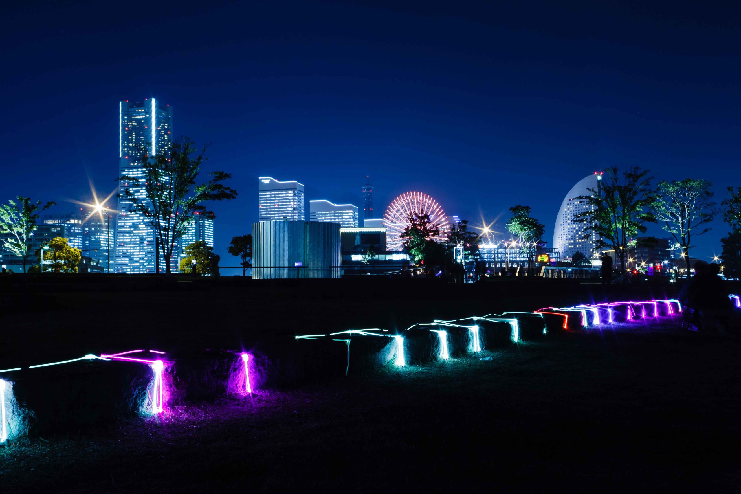 横浜の夜景を背景に、紫や白の光で縁取られた石のベンチ型イルミネーション「ChAir」
