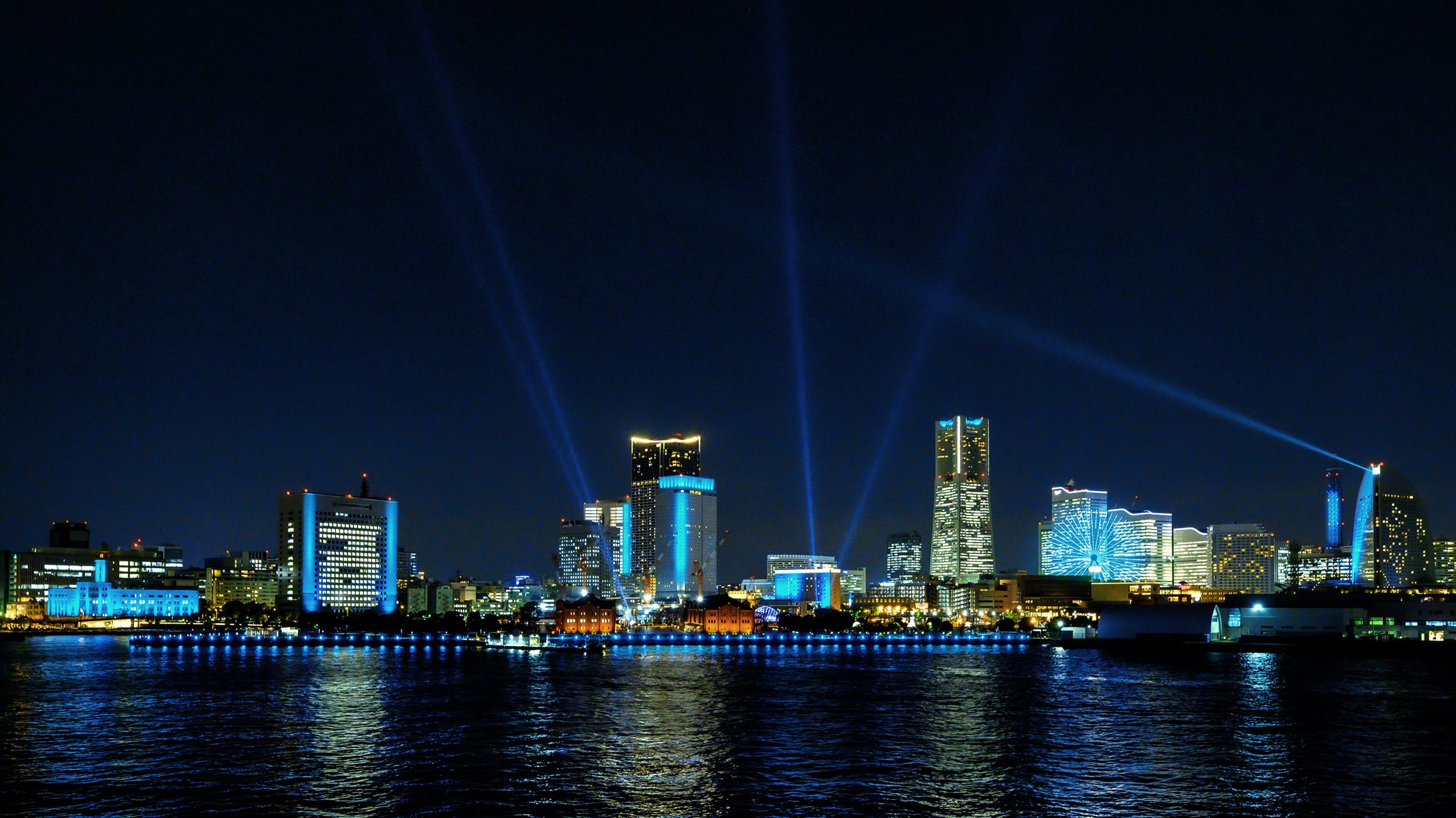 横浜の夜景に、複数のサーチライトが交差して伸びる「ヨルノヨ 2021 – FLOW –」の光の演出
